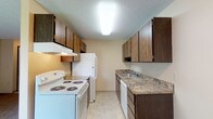 Located at 10015 N Colfax Rd in Spokane, Washington, Unit 44 is a single-floor residence thoughtfully designed for comfortable everyday living. The layout flows efficiently through well-defined spaces, each finished with practical materials and neutral tones throughout.

The galley-style kitchen is equipped with dark wood cabinetry offering generous upper and lower storage, granite-patterned countertops, a stainless steel sink, and white appliances including an electric range, refrigerator, and dishwasher. Light tile flooring completes the clean, functional aesthetic.

The living area is carpeted and bathed in natural light, featuring a sliding glass door that opens to a private balcony with outdoor views — an inviting extension of the living space. A baseboard heating system runs along the walls, providing consistent warmth throughout the unit.

The bedroom is a comfortable, carpeted retreat with a window allowing natural light, a baseboard heater, and direct access to a spacious walk-in closet. The adjoining bathroom features a wide vanity with dark wood cabinetry, a large mirror, tile flooring, and a full soaking tub with a tiled shower surround.

Textured ceilings are present throughout, and the entryway provides a welcoming transition into the main living space.