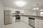 Located at 996 Paisley Rd, Suite 511 in Guelph, Ontario, this well-appointed one-bedroom, one-bathroom unit offers a thoughtfully designed open-concept layout across a single floor. The kitchen is a functional highlight, featuring white shaker-style cabinetry, grey composite countertops, stainless steel appliances including a refrigerator, stove, built-in microwave, and dishwasher, along with light tile flooring. A peninsula with pendant lighting connects the kitchen to the combined dining and living area, which is finished with warm wood-tone laminate flooring and large sliding glass doors that flood the space with natural light and lead to a private balcony with open outdoor views. The bedroom is a comfortable size, offering mirrored sliding closet doors and the same laminate flooring, with easy access to the main living area. The bathroom includes a full soaker tub with chrome fixtures. A dedicated in-unit laundry area houses a full-sized top-load washer and dryer, adding everyday convenience. Neutral tones and clean finishes throughout create a bright, modern ambiance suited for comfortable living.