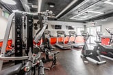 Located at 28 Forest Dr in Springfield, NJ, this fitness center — branded as Short Hills Fit — offers a thoughtfully designed, single-floor workout facility built to support a comprehensive exercise experience. The space features a bold, industrial-inspired aesthetic, with dark exposed ceilings accented by recessed LED lighting panels and visible ductwork, creating a modern and energetic atmosphere. Vivid red accent walls contrast against neutral gray tones, lending the space a dynamic visual character throughout.

The cardio zone is well-appointed with multiple treadmills and stationary bikes positioned to maximize floor space, complemented by wall-mounted flat-screen televisions for entertainment during workouts. Natural light filters in through several windows and glass-paneled entry doors, offering views of the surrounding outdoor area and enhancing the overall brightness of the space. Rubber flooring throughout provides durability and safety underfoot.

The strength and functional training area includes a multi-station cable machine, rowing equipment, spinning bikes, and various free-weight and resistance apparatus. Floor-to-ceiling mirrors along one wall visually expand the space and allow members to monitor their form. Additional amenities include a reception or check-in station, restroom access, and ample room to move freely between equipment zones, making this facility a fully functional and welcoming fitness destination.