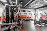 Located at 28 Forest Dr in Springfield, NJ, this fitness center — branded as Short Hills Fit — offers a thoughtfully designed, single-floor workout facility built to support a comprehensive exercise experience. The space features a bold, industrial-inspired aesthetic, with dark exposed ceilings accented by recessed LED lighting panels and visible ductwork, creating a modern and energetic atmosphere. Vivid red accent walls contrast against neutral gray tones, lending the space a dynamic visual character throughout.

The cardio zone is well-appointed with multiple treadmills and stationary bikes positioned to maximize floor space, complemented by wall-mounted flat-screen televisions for entertainment during workouts. Natural light filters in through several windows and glass-paneled entry doors, offering views of the surrounding outdoor area and enhancing the overall brightness of the space. Rubber flooring throughout provides durability and safety underfoot.

The strength and functional training area includes a multi-station cable machine, rowing equipment, spinning bikes, and various free-weight and resistance apparatus. Floor-to-ceiling mirrors along one wall visually expand the space and allow members to monitor their form. Additional amenities include a reception or check-in station, restroom access, and ample room to move freely between equipment zones, making this facility a fully functional and welcoming fitness destination.