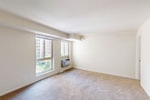 Located at 2120 Brooks Dr in District Heights, MD, this single-floor unit offers a thoughtfully organized layout that maximizes every square foot. The welcoming entrance opens into a carpeted living room bathed in natural light from a pair of large windows that frame views of the surrounding greenery and neighboring buildings. A wall-unit HVAC system ensures year-round comfort, while neutral cream-toned walls create a clean, bright atmosphere throughout.

The kitchen is positioned adjacent to the living area and is defined by a peninsula-style breakfast bar with a dark countertop, providing both a casual dining surface and a visual divider between spaces. Light wood cabinetry, a black refrigerator, and a black range give the kitchen a practical, functional character. Overhead flush lighting adds warmth to the cooking area.

A closet with louvered doors provides dedicated storage, and a hallway connects the main living spaces to the two bathrooms. The bathrooms are finished with white tile flooring, tiled shower surrounds, and clean white fixtures. One bathroom features an octagonal vanity mirror with overhead lighting above a white countertop sink, adding a modest decorative touch. The overall palette of soft neutrals and white finishes contributes to a cohesive, understated aesthetic throughout the unit.