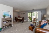 This single-floor residence offers a thoughtfully designed layout with comfortable living spaces and a consistent neutral color palette throughout. The living room serves as the heart of the home, featuring plush carpeting, warm beige walls, and ample space for relaxed seating arrangements. Natural light filters in through well-placed windows, contributing to the inviting ambiance of the room.

The adjacent dining area continues the carpeted flooring and is finished with soft gray walls, providing a calm and intimate setting for meals. A window overlooks lush greenery, bringing the outdoors in.

The galley-style kitchen is efficiently laid out with warm wood cabinetry, light countertops, a stylish tile backsplash, and tile flooring. It is equipped with full-size appliances and offers generous counter space for meal preparation.

The primary bedroom is generously sized, featuring dual sliding closets, soft carpet, and a window with peaceful wooded views. The second bedroom also enjoys natural light and tree-lined views, offering flexibility as a guest room or home office space.

Two bathrooms serve the residence — one with a single vanity, mirror, and shower, and a second with tile flooring and a shower-tub combination. The overall design is practical, cohesive, and well-maintained throughout.