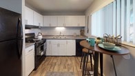 This thoughtfully designed single-floor residence offers a cohesive and comfortable living experience with modern finishes throughout. The kitchen is a standout feature, showcasing white shaker-style cabinetry that extends to the ceiling for ample storage, a subway tile backsplash, gray laminate countertops, and wood-look flooring. Black appliances including a gas range and dishwasher add a sleek contrast, while a window brings in natural light. A compact dining bar with stools provides a casual eating space within the kitchen area. The living room is inviting and open, anchored by a striking painted brick accent wall in soft gray. A sliding glass door floods the space with natural light and provides direct access to an outdoor patio area, offering pleasant outdoor views. Wood-look flooring continues seamlessly throughout. The bedroom is generously sized with soft gray walls, wood-look flooring, and a large window dressed with vertical blinds that allow for natural light. The bathroom is clean and functional, featuring a white vanity with gray countertop, a tub-shower combination, and wood-look flooring. Cool gray tones are carried consistently throughout the unit, creating a calm, unified aesthetic that ties each room together harmoniously.
