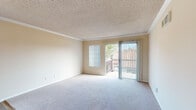 Located at 3901 Mesa Dr in Oceanside, California, this single-floor residence offers a well-organized layout with a warm, neutral color palette throughout. The living area features plush carpeting, crown molding, and a textured ceiling, with natural light streaming in through large windows and a sliding glass door that opens to a private balcony overlooking the surrounding neighborhood rooftops. A ceiling fan adds comfort to the adjacent space, where wood-look flooring transitions seamlessly from the living area into the kitchen. The kitchen is equipped with stainless steel appliances, including a refrigerator, range, microwave, and dishwasher, complemented by white cabinetry, light countertops, and a skylight that brightens the space. A breakfast bar connects the kitchen to the living and dining areas, enhancing the open flow. The bedrooms are carpeted and generously sized, with one featuring mirrored sliding closet doors and another equipped with a ceiling fan. Both bathrooms are finished with white fixtures, wide vanity mirrors, and full tub-shower combinations. Textured ceilings and consistent crown molding details tie the interior together, creating a cohesive and functional living environment.