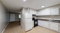 This single-floor home offers a practical and straightforward layout with a neutral, gray-toned color palette that flows consistently throughout. The kitchen is designed for functionality, featuring white cabinetry with ample upper and lower storage, dark countertops, a black gas range, a white refrigerator, and a built-in sink. Light tile flooring completes the kitchen space, which opens toward the main living areas. The full bathroom includes a tiled shower-tub combination, a window that brings in natural greenery views, a toilet, and a single vanity with a mirror — all finished in clean white tones with tile flooring. The bedrooms are carpeted and generously proportioned, each offering closet storage, including bi-fold closet doors for convenient access. The rooms are well-lit with windows framing outdoor greenery, providing a calm and pleasant atmosphere. The main living area is an open, carpeted space with a large window that allows natural light to fill the room. Throughout the home, clean white trim, consistent gray walls, and ceiling vents contribute to a cohesive and move-in-ready interior. The layout, as seen in the dollhouse view, is compact yet efficiently organized for comfortable everyday living.