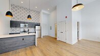 Located at 2801 S Pennsylvania St in Indianapolis, Indiana, this thoughtfully designed studio unit offers a compact yet efficient single-floor layout. Soaring ceilings amplify the sense of openness, while large windows along one wall flood the living area with natural light and offer views of the surrounding neighborhood. Light-toned hardwood-style flooring runs throughout, complementing the bright white walls and modern aesthetic.

The kitchen is a standout feature, centered around a peninsula with a striking veined quartz countertop and a matte black faucet over an undermount sink. Gray wood-toned cabinetry lines the walls, paired with a geometric-patterned tile backsplash that adds visual interest. Stainless steel appliances, including a refrigerator, range, and over-the-range microwave, complete the functional setup. A cluster of matte black pendant lights with warm gold interiors hang above, adding a contemporary design touch.

The bathroom is clean and functional, featuring a full tub/shower combination with matte black fixtures and hexagonal marble-look tile flooring. A dedicated closet provides storage, and a wall-mounted mini-split HVAC unit ensures climate control. The overall ambiance is modern, minimalist, and move-in ready.
