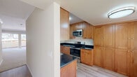 This single-floor residence offers a thoughtfully designed layout that balances functionality and comfort throughout. The galley-style kitchen is a standout feature, showcasing warm honey-toned wood cabinetry extending from floor to ceiling, dark granite countertops, and a full suite of stainless steel appliances including a refrigerator, electric range, over-the-range microwave, and dishwasher. Light wood-style flooring runs the length of the kitchen, adding a clean, modern contrast to the rich cabinetry. The spacious living area is finished with plush wall-to-wall carpeting, crown molding, and a ceiling fan, creating a comfortable and inviting atmosphere. Large sliding glass doors open to an outdoor balcony, flooding the room with natural light and providing pleasant exterior views. The bedrooms continue the carpeted flooring and are equipped with mirrored sliding closet doors that enhance the sense of space. The bathrooms are finished with updated white vanities featuring clean countertops, large mirrors, and wood-look tile flooring. One bathroom includes a tub-shower combination with sliding glass doors. The overall palette throughout the residence is neutral and warm, with soft beige tones creating a cohesive and move-in-ready environment.