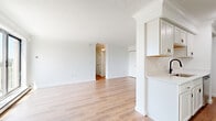 Located at 12000 Fairhill Rd in Cleveland, OH, this 3-bedroom, 2-bathroom unit offers a thoughtfully updated interior spread across a single floor. Light wood laminate flooring runs consistently throughout the space, creating a warm, cohesive feel. Crown molding adds a refined architectural detail in the living areas and bedrooms.

The combined kitchen and living room area forms the heart of the unit. The kitchen features white shaker-style cabinetry extending to the ceiling, light countertops, a black matte sink fixture, and stainless steel appliances including a full-size refrigerator. The adjacent living area is open and bright, with a large sliding glass door that floods the room with natural light and provides access to a balcony with exterior views.

Each of the three bedrooms is well-proportioned, with the spacious primary bedroom offering a closet and ample room. The secondary bedrooms feature windows with blinds that bring in natural light, along with baseboard heating and wall-unit air conditioning for year-round comfort.

The two bathrooms are cleanly finished with white vanities accented by matte black and brushed gold hardware, framed mirrors, and walk-in shower stalls. One bathroom features a sleek sliding glass shower door, while the other offers an open shower design. The overall aesthetic is clean, modern, and move-in ready.