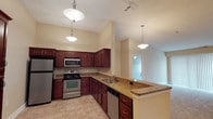 This single-floor residence is designed with a practical and cohesive aesthetic throughout. The kitchen serves as a central highlight, showcasing rich dark-wood cabinetry, granite countertops, and a full suite of stainless steel appliances, including a refrigerator, electric range, built-in microwave, and dishwasher. A peninsula with additional counter space and cabinetry extends the kitchen's functionality, while pendant lighting adds a polished finishing touch. The vaulted ceiling in the kitchen and adjacent dining area contributes to an open, airy atmosphere.

The living areas are finished with neutral-toned carpet and warm beige walls, creating a versatile and welcoming environment. Multiple bedrooms offer generous proportions, each featuring ceiling fans, natural light from windows, and plush carpeting. The layout connects bedrooms conveniently to the bathrooms.

Two bathrooms are present in the unit. One features a walk-in shower with a glass door and dark granite vanity, while the second includes a full soaking tub/shower combination and a matching dark-wood vanity with granite countertop. Both bathrooms are finished with tile flooring, providing a clean and durable surface throughout.