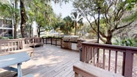 Located at 997 Johnnie Dodds Blvd in Mount Pleasant, South Carolina, this single-level outdoor space offers a welcoming and functional environment ideal for gathering and entertaining. The expansive wooden deck serves as the centerpiece of the space, constructed with warm-toned planking and framed by sturdy railings that define the area while maintaining open sightlines to the surrounding landscape.

A standout feature of this outdoor space is the built-in grilling station, which includes multiple stainless steel gas grills set into a stone-clad base. This setup is well-suited for hosting outdoor cookouts and social events. Seating areas are integrated throughout the deck, providing ample room for guests to relax and gather.

The natural setting is a defining characteristic of this space. Towering palm trees and mature live oaks draped in Spanish moss create a canopy that adds shade and a distinctly Lowcountry aesthetic. The lush greenery surrounding the deck lends a serene, park-like atmosphere that reflects the charm of the coastal South Carolina region.

In the background, additional outdoor amenities such as umbrella-shaded seating areas are visible, suggesting this deck is part of a broader outdoor complex. A classic lamp post adds a refined, welcoming touch to the overall ambiance, making this a well-appointed and inviting outdoor destination.
