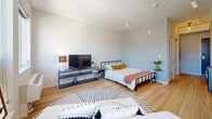 Located at 337 Seventh St W in Saint Paul, Minnesota, this one-bedroom, one-bathroom unit offers a compact yet efficiently designed single-floor layout. The open-concept living area is filled with natural light streaming through large windows that frame views of the surrounding cityscape, creating an airy and inviting atmosphere. Light wood flooring runs throughout, lending warmth and continuity to the space.

The main living area seamlessly integrates the living, sleeping, and kitchen zones. The kitchen is outfitted with light wood cabinetry, stainless steel appliances including a full-size refrigerator and built-in microwave, a stainless steel sink, and an in-unit washer, offering strong functionality within a compact footprint. Track lighting overhead brightens the kitchen area effectively.

The sleeping area is generously proportioned relative to the overall unit size, accommodating a full bedroom setup with room for furnishings. Clean white walls and soft, neutral tones contribute to a calm and modern aesthetic throughout.

The bathroom features warm wood-tone flooring consistent with the rest of the unit, a floating white vanity with an undermount sink, a shower/tub combination, and crisp white walls that keep the space feeling clean and bright. A hallway connects the main living area to the bathroom, providing a functional transition between spaces.