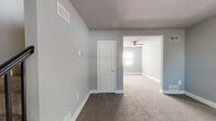 This two-floor space is designed with a consistent, neutral aesthetic, featuring light gray walls and warm white trim throughout. Soft carpet flooring flows across the living areas and bedrooms, creating a cohesive and comfortable feel from room to room.

The kitchen is equipped with warm honey-toned wooden cabinetry, offering ample upper and lower storage. A gas range and sink with a granite-style countertop are positioned near a window, allowing natural light to brighten the workspace. The floor features neutral tile, providing a practical contrast to the carpeted areas.

Multiple rooms across both floors share a similar layout, each painted in cool gray tones with plush carpet underfoot. Windows fitted with horizontal blinds are present in several rooms, allowing controlled natural light and outdoor views. Ceiling fans are visible in select areas, adding both function and airflow. One room features a dedicated closet door, suitable for use as a bedroom.

The bathroom includes a full-size soaking tub with tiled surround, a toilet, and a vanity with countertop storage. Tile flooring and partial wall tiling give the space a clean, utilitarian finish.

Overall, the space maintains a clean, move-in-ready appearance with functional layouts across both floors.