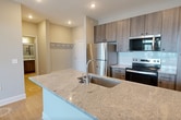This 690-square-foot, one-bedroom, one-bathroom apartment at Unit 1501, 80 Lawrenceville Suwanee Rd, Lawrenceville, GA 30044, offers a well-planned single-floor layout with modern finishes throughout. The open-concept kitchen and living area serves as the heart of the unit, featuring a large granite-topped island with an undermount sink, stainless steel appliances including a refrigerator, electric range, and built-in microwave, complemented by contemporary wood-toned cabinetry and a classic subway tile backsplash. Recessed lighting and light wood-style flooring enhance the kitchen's bright, clean aesthetic. The living room extends naturally from the kitchen, bathed in natural light through large windows and a glass door, and is equipped with a ceiling fan. The 160-square-foot primary bedroom offers plush carpeting, dual windows with outdoor views, and a ceiling fan, with access to a dedicated walk-in closet featuring multi-tier wire shelving. The full bathroom includes a wood-toned vanity with granite countertops, an undermount sink, and matching light wood flooring. A hallway connects the living areas to the private spaces, completing this efficiently designed modern apartment.