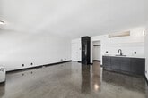 Located at 745 Garland Ave in the heart of Los Angeles, this thoughtfully designed one-bedroom, one-bathroom unit offers a compact yet functional layout across a single floor. The main living area is the focal point of the space, featuring striking polished concrete floors that reflect light and lend an industrial-modern character throughout. Large windows along one wall frame open city views of the Los Angeles skyline, flooding the space with natural light and creating an airy, open atmosphere.

The kitchen area is integrated into the main living space, featuring sleek navy-blue cabinetry with matte black hardware, a white countertop, and a matte black sink faucet — a stylish and cohesive design choice. A full-size refrigerator with overhead cabinetry provides practical storage within the compact footprint.

The bedroom is generously proportioned relative to the overall unit size, offering ample room for furnishings. A dedicated closet provides additional storage. The bathroom showcases a clean, minimalist aesthetic with white square floor tiles, white walls, a wall-mounted mirror, and matte black fixtures and accessories that echo the design language found throughout the unit. A wide vanity with a vessel sink completes the bathroom's modern look.