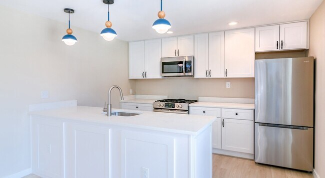 Mejora tu estilo de vida en Lakeshore Preserve, donde esta moderna cocina cuenta con elegantes gabinetes blancos, elegantes lámparas colgantes y electrodomésticos de alta gama. ¿Listo para hacer realidad este sueño culinario? ¡Programa tu visita hoy mismo! - Lakeshore Preserve