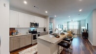This well-appointed single-floor residence showcases a thoughtfully designed open-concept layout that seamlessly connects the kitchen, dining, and living areas. Rich hardwood-style flooring runs throughout, lending warmth and continuity to every room.

The kitchen is a standout feature, outfitted with stainless steel appliances, including a range, microwave, and French door refrigerator. Cabinetry combines crisp white upper cabinets with warm wood-toned lower cabinets, accented by a classic subway tile backsplash. A generously sized granite island with a built-in sink and bar seating serves as both a functional workspace and a social hub.

The open living area offers a bright, welcoming atmosphere, benefiting from natural light through large windows dressed with patterned drapes. The space flows naturally into multiple bedrooms, each with its own distinct character. The primary bedroom features pendant lighting and ample natural light, while a second bedroom is distinguished by a bold teal accent wall. A spacious walk-in closet provides generous storage with multi-tiered shelving.

The bathroom includes a granite-topped vanity, a soaking tub with shower, and hardwood-style flooring, maintaining the cohesive, contemporary aesthetic found throughout the residence.