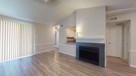 This single-floor residence offers a thoughtfully designed layout with a warm, neutral color palette and light wood-style flooring that flows consistently throughout the living areas and bedrooms. The living room serves as the heart of the home, highlighted by vaulted ceilings that enhance the sense of openness and a striking fireplace framed by dark tile surround and a clean white mantel. A pass-through opening connects the living area to the kitchen, which features white shaker-style cabinetry, sleek gray countertops, and stainless steel appliances including an electric range and over-the-range microwave. A dedicated entry foyer with overhead lighting provides a welcoming arrival experience. The bedroom is generously proportioned, fitted with a ceiling fan, a window with blinds for natural light, and direct access to a closet. The space includes two bathrooms: one with classic white tile surrounding a tub-shower combo, and a second, more updated bath featuring marble-look tile accents, wood-toned cabinetry, and wood-style flooring. Large vertical blinds in the living area allow for flexible light control. The overall ambiance is clean, bright, and move-in ready, with a cohesive modern-neutral aesthetic throughout.