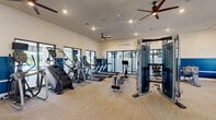 The Sanibel Straits Fitness Center at 16100 Myriad Lane in Fort Myers, Florida, is a thoughtfully designed, single-floor facility offering a full suite of exercise equipment and amenities. The interior features a neutral-toned carpet floor, recessed lighting, and multiple ceiling fans that maintain a comfortable environment throughout the space. A bold two-tone color scheme — crisp white upper walls paired with deep navy blue lower walls — gives the gym a clean, modern aesthetic, reinforced by the prominently displayed Sanibel Straits branding logo.

The main floor houses an extensive selection of Matrix-branded cardio machines, including treadmills, ellipticals, stair climbers, and a stationary bike, as well as a rowing machine. A central multi-functional cable machine serves as a focal point for strength training, complemented by a dedicated functional training area equipped with a red power rack, resistance bands, battle ropes, kettlebells, medicine balls, and stability balls. Flat benches and additional weight equipment round out the strength zone. Large windows along the perimeter allow natural light to filter in and provide outdoor views. Wall-mounted mirrors enhance the sense of openness, making this fitness center a well-equipped and inviting space for a full-body workout.