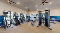 The Sanibel Straits Fitness Center at 16100 Myriad Lane in Fort Myers, Florida, is a thoughtfully designed, single-floor facility offering a full suite of exercise equipment and amenities. The interior features a neutral-toned carpet floor, recessed lighting, and multiple ceiling fans that maintain a comfortable environment throughout the space. A bold two-tone color scheme — crisp white upper walls paired with deep navy blue lower walls — gives the gym a clean, modern aesthetic, reinforced by the prominently displayed Sanibel Straits branding logo.

The main floor houses an extensive selection of Matrix-branded cardio machines, including treadmills, ellipticals, stair climbers, and a stationary bike, as well as a rowing machine. A central multi-functional cable machine serves as a focal point for strength training, complemented by a dedicated functional training area equipped with a red power rack, resistance bands, battle ropes, kettlebells, medicine balls, and stability balls. Flat benches and additional weight equipment round out the strength zone. Large windows along the perimeter allow natural light to filter in and provide outdoor views. Wall-mounted mirrors enhance the sense of openness, making this fitness center a well-equipped and inviting space for a full-body workout.