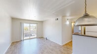 Located at 3946 Via Rosa in San Marcos, California, this single-floor, two-bedroom, one-bathroom residence offers a practical and well-organized layout. The living area features light wood-look flooring and is bathed in natural light, with a sliding glass door opening to a private balcony that overlooks surrounding greenery. The kitchen flows seamlessly from the living space, separated by a peninsula counter with an overhead pendant light. It is outfitted with white cabinetry, stone-toned countertops, a double stainless steel sink, and white appliances including a range, over-the-range microwave, and refrigerator. Both bedrooms are carpeted and feature mirrored sliding closet doors and windows with vertical blinds that invite natural light. The primary bedroom connects conveniently to the shared bathroom, which includes a full tiled tub-shower combo, safety grab bars, and wood-look flooring. A hallway connects the main living areas to the bedrooms and bathroom, providing a clear and functional flow throughout the home. The clean, neutral color palette of white walls and warm flooring tones creates a bright, cohesive ambiance throughout the entire residence.