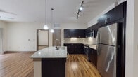 This well-appointed single-floor residence offers a thoughtfully designed open-concept layout that seamlessly connects the kitchen and living areas. The kitchen is a standout feature, showcasing dark espresso cabinetry that extends to the ceiling, sleek granite countertops, and a mosaic tile backsplash. A large center island with an integrated sink and pendant lighting provides both additional prep space and a casual dining option. Stainless steel appliances, including a refrigerator, range, and microwave, complete the kitchen's modern aesthetic. Track lighting and under-cabinet lights enhance functionality throughout.

The living area is generously sized with warm hardwood-style flooring and a ceiling fan, creating a comfortable and inviting atmosphere. Bedrooms are carpeted for added comfort, with one bedroom offering dual windows that bring in natural light. The walk-in closet provides ample storage with wire shelving systems.

The bathrooms feature granite-topped dark vanities, wood-look flooring, and are equipped with accessibility grab bars. A dedicated in-unit laundry room with a washer adds everyday convenience. Throughout the residence, consistent finishes and a neutral color palette create a cohesive, modern living environment.