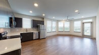 This contemporary single-floor residence in Carrollton, Texas offers a thoughtfully designed open-concept layout that seamlessly connects the kitchen and living areas. The kitchen is well-appointed with dark espresso cabinetry, a tile backsplash, stainless steel appliances including a refrigerator, dishwasher, range, and microwave, along with a double-basin sink beneath a window. Hardwood-style flooring flows throughout the main living spaces, lending warmth and visual continuity. The expansive living area is bathed in natural light from a generous bank of windows overlooking greenery, and is complemented by a ceiling fan overhead. The bedroom features plush carpeting, a ceiling fan, and corner windows that invite soft, natural light. A spacious walk-in closet with multiple hanging rods and shelving provides excellent storage. The primary bathroom is elegantly finished with dark wood vanity cabinetry, a wide dual-sink countertop, a large mirror, and a soaking tub with white subway tile surround. A second bathroom mirrors this clean aesthetic with white tile and a tub-shower combo. Recessed lighting throughout and neutral tones across all rooms contribute to a bright, modern ambiance suited for comfortable everyday living.