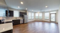 This contemporary single-floor residence in Carrollton, Texas offers a thoughtfully designed open-concept layout that seamlessly connects the kitchen and living areas. The kitchen is well-appointed with dark espresso cabinetry, a tile backsplash, stainless steel appliances including a refrigerator, dishwasher, range, and microwave, along with a double-basin sink beneath a window. Hardwood-style flooring flows throughout the main living spaces, lending warmth and visual continuity. The expansive living area is bathed in natural light from a generous bank of windows overlooking greenery, and is complemented by a ceiling fan overhead. The bedroom features plush carpeting, a ceiling fan, and corner windows that invite soft, natural light. A spacious walk-in closet with multiple hanging rods and shelving provides excellent storage. The primary bathroom is elegantly finished with dark wood vanity cabinetry, a wide dual-sink countertop, a large mirror, and a soaking tub with white subway tile surround. A second bathroom mirrors this clean aesthetic with white tile and a tub-shower combo. Recessed lighting throughout and neutral tones across all rooms contribute to a bright, modern ambiance suited for comfortable everyday living.