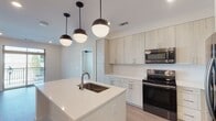 Located at 3908 University Dr in Durham, NC, this single-floor residence showcases a thoughtfully designed modern interior with clean lines and contemporary finishes throughout. The open-concept kitchen serves as the heart of the home, featuring a large central island with a built-in sink and crisp white quartz countertops. Light wood-toned cabinetry extends to the ceiling, providing generous storage, while stainless steel appliances — including a French door refrigerator, electric range, and over-the-range microwave — complete the space. Stylish matte black pendant lighting adds a striking contrast overhead, and light hardwood-style flooring ties the kitchen and common areas together seamlessly. The bedrooms offer plush carpeting, ceiling fans, and multiple windows that invite natural light and outdoor views. The primary bathroom features wood-grain vanity cabinetry with a granite countertop, matte black hardware, and direct access to a walk-in closet. A secondary bathroom includes a full soaking tub and shower combination with elegant marble-style tile surround and coordinating matte black fixtures. Together, these details create a cohesive, modern aesthetic that is both functional and visually refined.