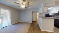 This single-story space offers a practical, well-appointed layout designed for comfortable everyday living. The main living area is a versatile open space finished with a combination of wood-look flooring and plush carpet, delineating distinct functional zones. A ceiling fan with a light kit overhead provides both ventilation and ambient lighting, while a textured ceiling adds a classic touch throughout. A sliding glass door floods the space with natural light and provides access to the outdoors.

The entry foyer transitions seamlessly into the living area, featuring the same dual-flooring combination and neutral gray walls. The galley-style kitchen is efficiently designed with white shaker cabinetry lining both sides, granite-look countertops, a mosaic tile backsplash, and black appliances including a range and refrigerator. A peninsula counter opens toward the living space, enhancing the sense of connectivity.

The bedroom is carpeted and bright, benefiting from a window fitted with horizontal blinds that allow for natural light control. The bathroom features wood-look flooring, a soaking tub with a marble-style tiled surround accented by a decorative mosaic border, and clean, neutral finishes throughout.