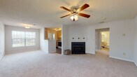 This single-story home offers a thoughtfully designed layout with a comfortable, functional flow throughout. The spacious living room serves as the heart of the space, featuring plush wall-to-wall carpeting, a ceiling fan with light fixture, and a classic tiled fireplace with a white mantle as a central focal point. A large window floods the room with natural light, while an open pass-through connects seamlessly to the kitchen, enhancing the sense of openness. The galley-style kitchen is efficiently arranged with light wood cabinetry, white countertops, and dark hardwood-style flooring. It is equipped with a coil-top electric range, dishwasher, and under-cabinet range hood, with an octagonal accent window adding a charming architectural detail. A door from the kitchen leads to an additional adjoining space. The bedrooms continue the carpeted aesthetic, each outfitted with ceiling fans and windows that invite natural light. One bedroom features a door leading to an outdoor area, providing easy exterior access. A walk-in closet adds practical storage. The bathroom includes a full tub and shower combination, a wood-finish vanity, and durable hardwood-style flooring. Throughout the home, neutral tones and consistent finishes create a clean, cohesive ambiance.