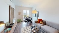 This thoughtfully designed single-floor residence offers a cohesive open-concept layout that seamlessly connects the living, dining, and kitchen areas. Wood-look flooring runs throughout, providing a warm, consistent foundation across the space.

The kitchen is outfitted with stainless steel appliances — including a refrigerator, electric range, and over-the-range microwave — complemented by light wood cabinetry, white quartz-style countertops, and a classic subway tile backsplash. The dining area is positioned adjacent to a large floor-to-ceiling window that frames sweeping urban views, including a prominent bridge in the distance. The bright living area continues the open feel with generous natural light.

The bedroom features a striking teal accent wall, a window with the same expansive urban views, and direct access to a dedicated laundry area equipped with a full-size stacked washer and dryer alongside built-in shelving. The bathroom includes a wood-tone vanity with an illuminated mirror, a tub-shower combination, and hardwood-style flooring. The overall aesthetic throughout is clean, modern, and well-appointed.