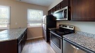 Located at 37 Cinema Dr in Lansing, NY, this single-floor unit offers a practical and well-appointed layout throughout. The kitchen is outfitted with dark espresso cabinetry, granite-style countertops, and a full suite of stainless steel appliances, including a range, over-the-range microwave, and refrigerator. Light hardwood-style flooring and a window overlooking greenery contribute to a bright, functional cooking space.

The living area is generously sized, featuring plush wall-to-wall carpeting and neutral-toned walls. A sliding glass door connects the space directly to a private balcony, allowing natural light to flow in and providing outdoor access. The bedroom spaces are also carpeted and finished in warm neutral tones, each offering closet storage—one with a double-door closet and another with a walk-in style closet. Windows in the bedrooms admit natural light and views of the surrounding area.

The bathroom includes a tiled tub-shower combination with white tile surround, a vanity with a white sink, tile flooring, and chrome towel bars, delivering a clean and functional design. Overall, the unit presents a cohesive, move-in-ready aesthetic with consistent finishes throughout.