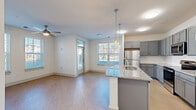 Located at 2050 Stanford Ln in Newport News, Virginia, this well-appointed single-floor home offers three bedrooms, two bathrooms, and a thoughtfully designed layout. The open-concept kitchen and living area serves as the heart of the home, featuring sleek gray cabinetry, granite countertops, a central island with pendant lighting, stainless steel appliances, and light wood-style flooring. Multiple windows flood the space with natural light and provide views of the surrounding neighborhood. The bedrooms are carpeted for comfort, with the primary bedroom offering a spacious walk-in closet equipped with wire shelving and built-in storage. Both bathrooms are finished with granite-topped gray vanities and built-in shelving; one includes a tub-shower combination with brushed gold fixtures and tile surround. A dedicated in-unit laundry room houses a stacked washer and dryer. Four hallways connect the rooms efficiently, maintaining a clean, open flow throughout. The interior is finished in a neutral white and gray palette, creating a bright, modern ambiance. A ceiling fan in the living area and consistent light wood-style flooring in common areas further enhance the cohesive, contemporary feel of this functional and comfortable home.