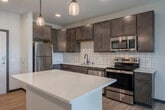 This thoughtfully designed 1-bedroom, 1-bathroom unit offers a functional and modern living experience across a single floor. The open-concept kitchen and living area serves as the heart of the space, featuring rich dark-stained cabinetry, a classic white subway tile backsplash, and a full suite of stainless steel appliances including a refrigerator, electric range, microwave, and dishwasher. A central kitchen island with a crisp white quartz countertop provides additional prep space and casual dining options, illuminated by stylish pendant lights overhead. Light wood-style flooring flows throughout the main living areas, enhancing the bright and airy atmosphere. The living room opens directly to a private balcony through a sliding glass door dressed with vertical blinds, offering pleasant outdoor views and natural light. A ceiling fan adds comfort to both the living room and bedroom. The spacious primary bedroom is carpeted for warmth and comfort, featuring large windows that frame outdoor greenery and allow for generous natural light. The full bathroom includes a soaking tub with shower combination and wood-style flooring, maintaining a clean and cohesive aesthetic throughout. A dedicated closet completes this efficiently designed unit.