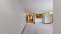 Located at 400 S Edwards Blvd in Lake Geneva, WI, this 2-bedroom, 1-bathroom single-floor residence offers a practical and comfortable layout. The open kitchen and living room area is anchored by warm oak cabinetry, light granite-style countertops, and a full suite of black appliances including a refrigerator, electric range, and dishwasher. Durable wood-look vinyl flooring runs throughout the kitchen, complemented by a ceiling fan overhead and a large closet providing ample storage. The spacious living room features plush wall-to-wall carpeting, neutral gray walls, a wall-mounted A/C unit, and a wood-trimmed window that fills the room with natural light. Both bedrooms are carpeted and include ceiling fans and windows with natural light; the primary bedroom offers generous proportions and a sliding wood-panel closet door. The bathroom is cleanly appointed with vinyl plank flooring, a white vanity, and a full tub-shower combination. Dark wood baseboards throughout the unit add a consistent, grounded aesthetic. The single-floor design ensures easy accessibility, and the overall layout is efficient and well-organized, making this a functional residence in the heart of Lake Geneva.