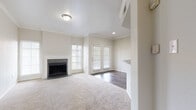 This single-story space is designed with a neutral, light-filled palette throughout, creating a clean and cohesive aesthetic. The living area serves as the centerpiece of the layout, featuring plush carpet flooring, crown molding, and a fireplace framed by a dark tile surround and white mantel. Natural light enters through multiple windows fitted with plantation-style blinds, and a set of French doors provides direct outdoor access while enhancing the open feel of the space.

Adjacent to the living area, the dining and entry zone features rich, dark hardwood-style flooring that transitions smoothly between spaces. A half-wall with a dark granite countertop edge connects this area to the kitchen, which is equipped with white raised-panel cabinetry, bold dark granite countertops, stainless steel appliances including an electric range and over-the-range microwave, and matching hardwood-style flooring.

The bedrooms are carpeted and generously proportioned, offering tall ceilings and windows that bring in natural light. The primary bedroom connects to a walk-in closet with built-in shelving and an en-suite bathroom featuring white cabinetry, dark granite counters, wood-style flooring, and a tiled tub-shower combination with a decorative accent tile border.