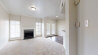 This single-story space is designed with a neutral, light-filled palette throughout, creating a clean and cohesive aesthetic. The living area serves as the centerpiece of the layout, featuring plush carpet flooring, crown molding, and a fireplace framed by a dark tile surround and white mantel. Natural light enters through multiple windows fitted with plantation-style blinds, and a set of French doors provides direct outdoor access while enhancing the open feel of the space.

Adjacent to the living area, the dining and entry zone features rich, dark hardwood-style flooring that transitions smoothly between spaces. A half-wall with a dark granite countertop edge connects this area to the kitchen, which is equipped with white raised-panel cabinetry, bold dark granite countertops, stainless steel appliances including an electric range and over-the-range microwave, and matching hardwood-style flooring.

The bedrooms are carpeted and generously proportioned, offering tall ceilings and windows that bring in natural light. The primary bedroom connects to a walk-in closet with built-in shelving and an en-suite bathroom featuring white cabinetry, dark granite counters, wood-style flooring, and a tiled tub-shower combination with a decorative accent tile border.