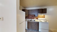 Located in Fairway, this single-floor residence offers a practical and comfortable layout with several notable design details throughout. The kitchen serves as a standout space, featuring rich dark wood cabinetry — both upper and lower — paired with a striking exposed red brick backsplash that adds warmth and character. White appliances, including a refrigerator, electric coil range, and dishwasher, complement the light countertops, while tile flooring provides a durable, easy-to-maintain surface. The living area is finished with wall-to-wall carpet in a neutral tone, creating a warm and inviting atmosphere. A large window allows natural light to fill the room, and a louvered closet door provides convenient storage nearby. The bedroom continues the carpeted flooring and neutral color palette, featuring its own window for natural light and a ceiling-mounted light fixture. The bedroom also includes closet space, keeping the room organized and functional. The bathroom is straightforward and clean, equipped with a full-size tub and shower combination, a toilet, and tile flooring that ties the space together. Throughout the residence, textured ceilings, white trim, and consistent neutral wall tones create a cohesive and understated aesthetic.