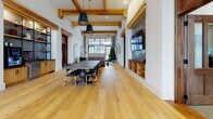 Located at 2500 Gault Way Dr in Summerville, South Carolina, this single-floor community clubhouse blends rustic warmth with modern sophistication throughout its expansive open layout. The entryway makes an immediate impression with soaring ceilings, floor-to-ceiling steel-framed windows, and oversized glass doors that flood the space with natural light while offering clear views of the surrounding community. Warm hardwood flooring runs throughout, complemented by exposed wood ceiling beams that add architectural character and a sense of craftsmanship.

The main gathering area is anchored by a large dark-toned communal table surrounded by sleek black chairs, ideal for group meetings or social events. A built-in brick-accented media wall with open shelving and a mounted flat-screen television serves as a focal point, combining function with design. Pendant lighting adds a refined industrial touch overhead.

A welcoming lounge area near the entrance features cognac leather chairs, a central pedestal table atop a patterned area rug, and curated artwork on crisp white walls. A large wood-framed mirror and console table add an elegant, residential feel. Additional rooms branch off the main hall through richly trimmed wood doorways, offering flexible spaces for various uses. Overall, the clubhouse exudes an inviting, upscale atmosphere rooted in thoughtful design.
