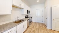 Located at 5895 Arbor Isle Way in Myrtle Beach, South Carolina, this single-floor residence offers a clean, contemporary design with a thoughtful layout throughout. The kitchen is a functional highlight, showcasing white shaker-style cabinetry, granite countertops, a classic subway tile backsplash, and a full suite of stainless steel appliances including a refrigerator, range, microwave, and dishwasher. A built-in wine rack adds a refined touch to the upper cabinetry. Light hardwood-style flooring runs through the kitchen and entry areas, creating a warm, cohesive aesthetic. The open living area is generously sized, featuring plush neutral carpeting, a ceiling fan with light fixture, and multiple windows dressed with horizontal blinds that invite ample natural light into the space. Additional doors throughout suggest well-organized closet and storage access. The bathroom is neatly finished with matching granite countertops, white cabinetry, a large vanity mirror, and a tub-shower combination set against clean white tile surround. The light wood-look flooring continues here, maintaining consistency throughout the home. Overall, the residence presents a bright, move-in-ready interior with modern finishes and a comfortable, functional flow.