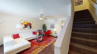 Located in Jacksonville, FL (32244), this two-story home offers a well-organized layout across two floors. The main level centers around a bright and inviting living room, featuring rich hardwood flooring, a ceiling fan, wainscoting, and a textured ceiling. The space is defined by an open, comfortable atmosphere with a carpeted staircase leading to the upper level. Adjacent to the living area, the dining space accommodates a round glass-top table beneath a pendant light, with a window allowing natural light to filter in. The kitchen is outfitted with white cabinetry, dark granite-style countertops, a double stainless steel sink, and black appliances including a gas range and refrigerator. A half bathroom on the main floor features hardwood flooring and slanted ceiling detail. Upstairs, the second floor includes carpeted rooms, one of which serves as a versatile flex space with built-in shelving and ample natural light. The full bathroom on this level is appointed with dark granite countertops, a tub-shower combination, a large mirror, and hardwood flooring. Throughout the home, the interior maintains a warm, neutral palette complemented by vibrant art pieces that add character and energy to each room.