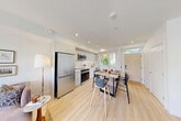 Located at 2650 41st Avenue East in Vancouver, BC, this thoughtfully designed two-bedroom, two-bathroom townhouse is spread across three well-proportioned floors. The contemporary exterior gives way to a bright, modern interior characterized by light hardwood flooring, clean white walls, and large windows that invite abundant natural light throughout.

The main floor hosts an open-concept kitchen and dining area, outfitted with sleek flat-front cabinetry, a white tile backsplash, stainless steel appliances including a range, microwave, and dishwasher, and a functional single-basin sink. A casual dining table sits adjacent to a window with greenery views. The living room on this level opens directly to a private outdoor patio through sliding glass doors, seamlessly connecting indoor and outdoor living.

The second floor features a secondary living room with a large window, a full bathroom with a soaking tub and shower combination, and a second bedroom with its own closet and natural light. The upper floor contains the primary bedroom, complete with a built-in closet, and a second full bathroom featuring a glass-enclosed walk-in shower, tiled surround, and frosted windows for privacy.

Multiple closets and staircases throughout the home ensure practical storage and easy flow between levels, making this a well-organized and comfortable urban residence.
