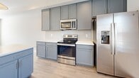 This two-story home in Clarksville, Tennessee offers a well-designed layout spread evenly across two floors. The main level features an open-concept living and kitchen area finished with light luxury vinyl plank flooring that extends throughout. The kitchen is outfitted with slate-gray cabinetry, white subway tile backsplash, light quartz countertops, stainless steel appliances including a range, microwave, and refrigerator, and a central island with pendant lighting overhead. A ceiling fan complements the spacious living area, which flows seamlessly from the kitchen. A half bathroom with hardwood-style flooring is conveniently located on the main floor. The entry foyer features a carpeted staircase leading to the upper level. Upstairs, two bedrooms are finished with plush carpet and ceiling fans. The generously sized primary bedroom includes a bank of windows that fill the room with natural light and ample closet space. A second well-proportioned bedroom also features a window and dedicated closet. The upper level includes two full bathrooms, one of which features gray cabinetry, a marble-style countertop, and a tiled tub-shower combination. Three closets provide substantial storage throughout the home.