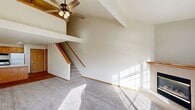 This two-story home is thoughtfully designed across two floors, with the majority of the living space situated on the main level. The living room is a standout feature, boasting soaring vaulted ceilings with exposed beam detailing and a ceiling fan that enhance the sense of openness and volume. Large windows flood the space with natural light, while a tiled fireplace provides a functional focal point. Carpeted flooring extends throughout the living areas, and a staircase with a wooden railing leads to the upper level. A door on the main floor provides direct access to an outdoor deck with wooded views.

The kitchen is well-equipped with warm-toned wood cabinetry, recessed lighting, a peninsula with ample counter space, and hardwood flooring. It flows conveniently alongside the main living area. The bathroom features light wood flooring, a full bathtub, and a wood-accented vanity.

The upper floor hosts the generously sized primary bedroom, featuring vaulted ceilings, a ceiling fan, and carpet flooring. An open loft-style landing with a wooden railing overlooks the living room below, adding architectural character. Two closets are distributed throughout the home, offering practical storage solutions.