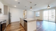 This single-floor residence showcases a contemporary design with a cohesive blend of modern finishes throughout. The open-concept kitchen serves as the centerpiece, featuring a large central island topped with speckled granite countertops, an undermount sink, and stylish pendant lighting overhead. Cabinetry combines crisp white uppers with warm wood-tone lowers, complemented by a white subway tile backsplash and a full suite of stainless steel appliances, including a refrigerator, range, microwave, and dishwasher. Wood-style plank flooring extends through the kitchen and living areas, adding warmth and visual continuity.

The living space is bright and open, benefiting from natural light through windows dressed with blinds and a sliding glass door with vertical blinds providing outdoor access. Bedrooms feature plush neutral carpeting and ceiling fans, each with windows offering natural light. The bathrooms are finished with granite-topped vanities, light wood cabinetry, and brushed nickel fixtures. One bathroom includes both a separate glass-enclosed shower and a tiled soaking tub, while another offers a tub-shower combination. Built-in overhead cabinetry provides additional storage. The overall ambiance is clean, bright, and move-in ready.