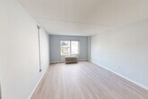 Located at 1850 Post Rd in Warwick, Rhode Island, this one-bedroom, two-bathroom unit offers a thoughtfully organized single-floor layout. The entrance opens into a corridor flanked by a closet, leading into the main living areas. Light wood-style flooring runs throughout, complementing the soft blue-gray wall tones and crisp white trim that define the unit's clean, modern aesthetic.

The living room is an open, well-lit space featuring a wall-mounted HVAC unit and a large window that invites natural light and outdoor views. It flows seamlessly from the entrance, creating a cohesive and airy feel. Adjacent to the living area is the combined dining and kitchen space, equipped with stainless steel appliances including a full-size refrigerator.

The generously sized primary bedroom continues the same light flooring and neutral palette, with a broad window overlooking the surrounding area, providing ample natural light and ventilation via an in-wall HVAC unit.

Both bathrooms are well-appointed with accessible features, including grab bars. One bathroom features a tub/shower with white subway tile surround, while the other includes a lighted vanity mirror, granite-topped floating sink, tiled flooring, and a tub — offering both functionality and a clean, modern finish throughout.