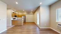 This single-floor unit offers a thoughtfully designed layout centered around an open-concept living and kitchen area. The kitchen is well-appointed with warm wood-tone flat-front cabinetry, white countertops, and a full suite of stainless steel appliances including a refrigerator, electric range, and over-the-range microwave. A peninsula with a built-in sink and breakfast bar separates the kitchen from the living area, which features durable luxury vinyl plank flooring and recessed lighting throughout. Natural light enters through a window with blinds and a glass-paned exterior door.

The unit includes two bedrooms, each carpeted and equipped with wall-mounted HVAC units and windows with blinds. One bedroom offers a more spacious feel, while the second serves well as a guest room or home office. A hallway connects the private areas of the unit, lined with closet access and panel doors.

Two bathrooms provide functional comfort. The full bath features a tub-shower combination, wood-tone vanity with white countertop, and vinyl plank flooring. The second bath offers a similarly styled vanity and toilet. Neutral beige wall tones and clean white trim create a cohesive, modern ambiance throughout the space.