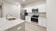 Located at 1151 Knob Hill Blvd in Georgetown, Indiana, this well-designed 2-bedroom, 2-bathroom single-floor home offers a clean, modern aesthetic throughout. The open-concept kitchen and living area serves as the heart of the home, showcasing white shaker-style cabinetry, granite countertops, stainless steel appliances, and a central island with a built-in sink — ideal for both cooking and entertaining. Light wood-look luxury vinyl flooring flows throughout the main living areas, complementing the neutral gray walls and crisp white trim.

The primary bedroom is a comfortable retreat with a ceiling fan, a window dressed with sheer curtains for natural light, and a dedicated closet with built-in shelving. The second bedroom features plush carpeting and soft neutral tones. Both bathrooms are well-appointed, with one featuring a tiled walk-in shower and granite vanity, and the other offering a full soaking tub. Recessed lighting throughout keeps the space bright and inviting.

A dedicated laundry area includes a full-size washer and dryer with overhead wire shelving for added storage. Two hallways connect the layout efficiently, and a closet provides additional storage. The overall ambiance is clean, contemporary, and move-in ready.