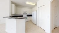 This two-story home offers a thoughtfully designed layout across two levels, combining practical functionality with comfortable living spaces. The kitchen is well-equipped, featuring white cabinetry, dark countertops, tile flooring, and white appliances including a refrigerator, electric range, microwave, and dishwasher, providing ample workspace and storage for everyday use. The main living area is bright and open, finished with light tile flooring and anchored by a white-railed staircase leading to the upper level. Large sliding glass doors flood the space with natural light and provide direct access to the outdoors. Upstairs, the bedrooms are carpeted and generously sized, with large windows offering pleasant views of surrounding greenery. One bedroom features a tray ceiling detail, adding an architectural touch. The primary suite includes a spacious walk-in closet with wire shelving systems for organized storage. The bathrooms are clean and well-appointed — one features a glass-enclosed shower with tile surround, while another includes a full tub-shower combination with white tile walls. Throughout the home, a neutral color palette of whites and warm beiges creates a bright, cohesive ambiance that feels open and inviting.