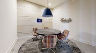 Located at 1801 Meridian St in Nashville, Tennessee, this single-floor amenity space blends modern design with functional versatility. The standout feature is a dedicated meeting room centered around a circular dark wood table surrounded by vibrant multicolored plaid swivel chairs, all anchored by a textured area rug. A bold navy pendant light hangs overhead, casting focused illumination over the workspace. One wall is clad in layered white panel detailing, adding depth and texture, while a "Nashville" marquee sign pays homage to the city's character. A wall-mounted display screen completes the room's collaborative setup.

Large, grid-paned glass walls and doors visually connect the meeting room to the surrounding common areas, creating a sense of openness and transparency throughout the space. Polished concrete floors extend through the corridors, lending an industrial-modern aesthetic that ties the areas together cohesively. Adjacent to the meeting room, a fitness center is visible through glass-panel doors, equipped with exercise machines and bathed in natural light from exterior windows. The overall design is clean and contemporary, with neutral white walls, recessed lighting, and thoughtful use of color accents that reflect both functionality and a distinctly Nashville-inspired personality.
